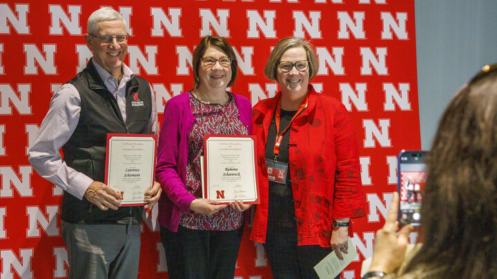 Three individuals standing in front of a red N back drop, with another individual taking their photo on a phone. 