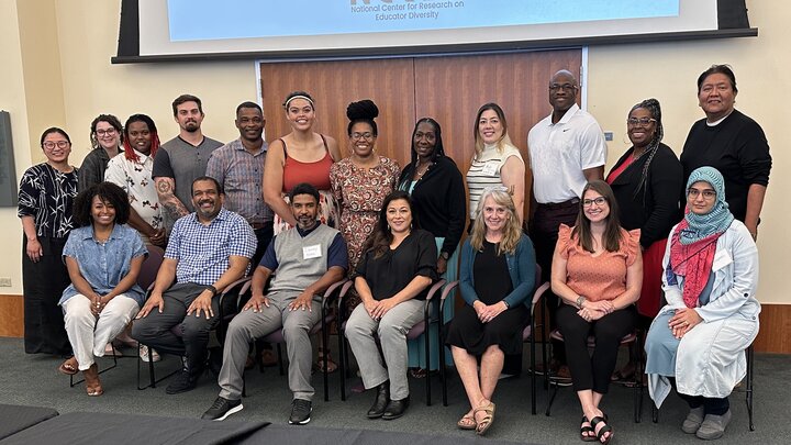 Two rows of people smile for a photo in front of a large projector screen. 