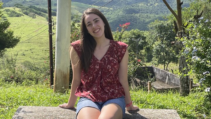 Julia Rossigno sits on a bench overlooking a vast green landscape. 