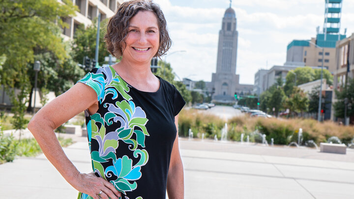 Julia Torquati stands smiling outdoors with the Nebraska State Capitol behind her. 