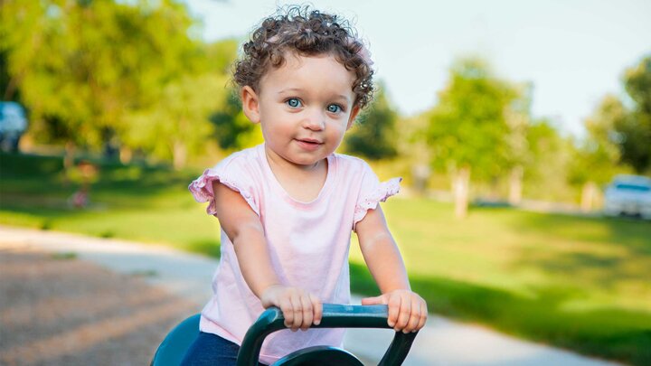 A young child wearing a pink shirt sits on playground equipment in an outdoor setting. 