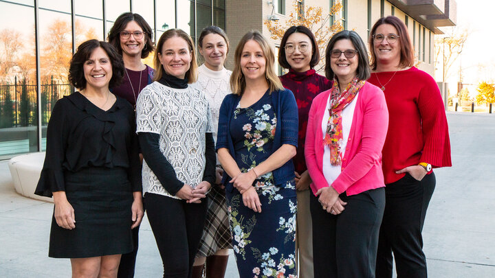 Eight individuals dressed in business clothing stand outdoors smiling for a photo. 