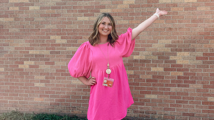 Paige Lindau poses with arm extended in front of a school