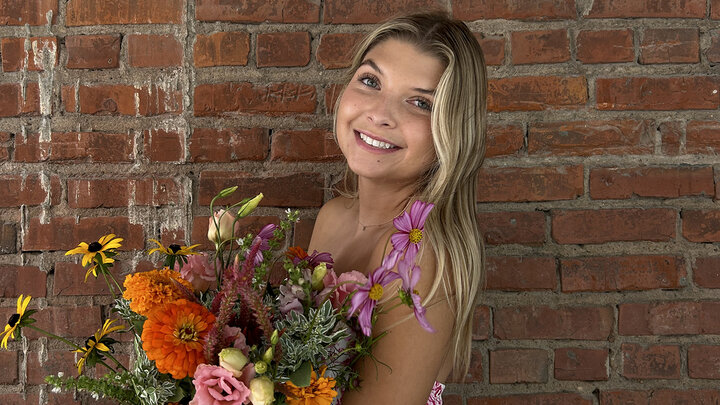 Kelsey Wathen holds a bouquet of flowers for a photo in front of a brick wall