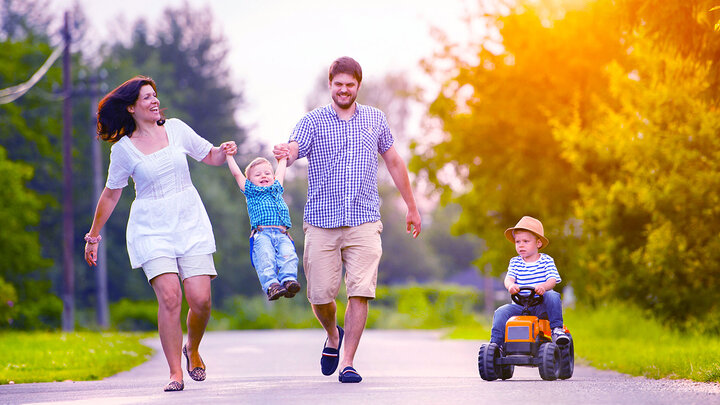 family walks down a sidewalk with one child driving a rideable toy