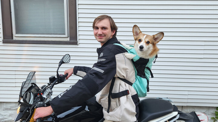 Breckin Killingsworth sits on a motorcycle with his dog in a carrier on his back