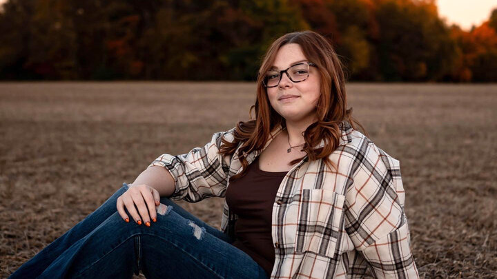 Taylor Dosier portrait image sitting in a field as the sun sets