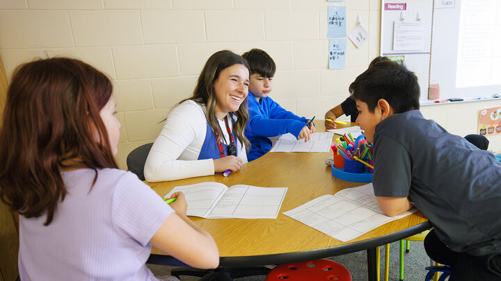 Rachel Morros helps four students at her desk during student teaching