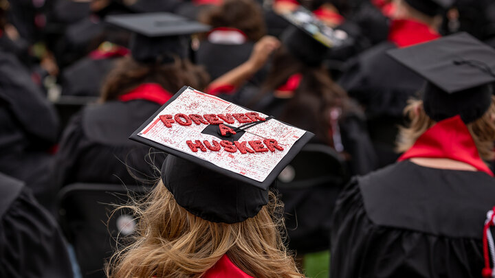 graduates seated at graduation with a mortar board decorated to say Forever A Husker