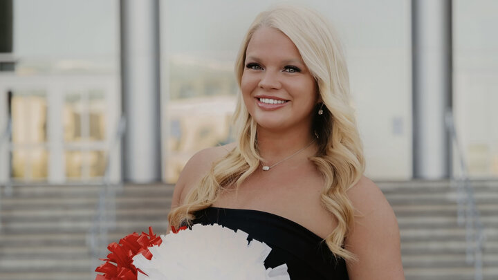 Ashley Goodyear stands outside Memorial Stadium holding red and white pom poms