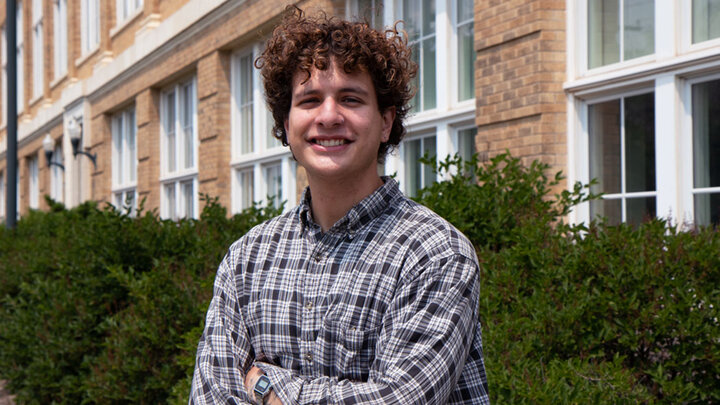 Jared Noetzel stands outside a building smiling with his arms crossed