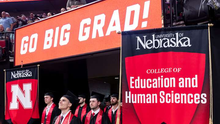 graduates entering Pinnacle Bank Arena next to College of Education and Human Sciences flag and under display board that reads Go Big Grad!