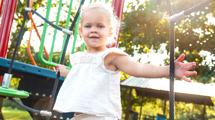 child looks at camera with slight smile while playing on a playground