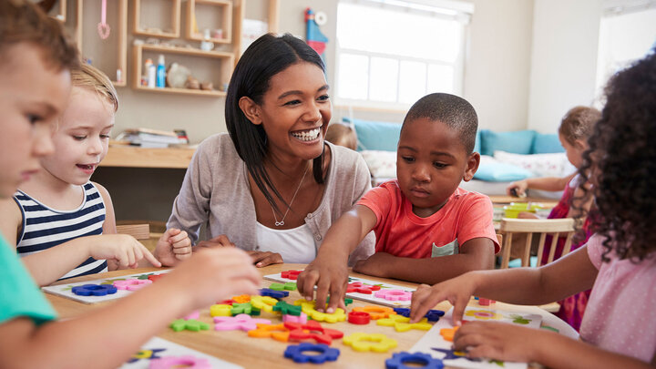 woman smiles while sitting at a table with children playing with shapes