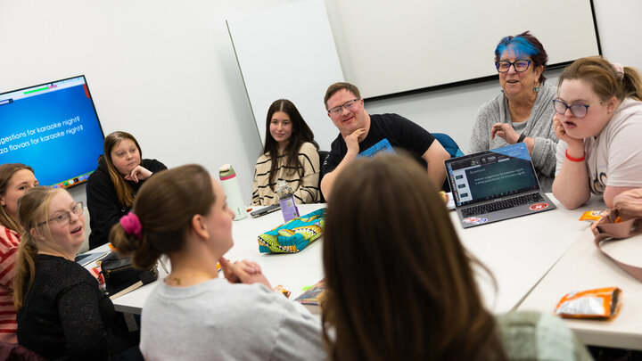Book club participants laugh and smile while discussing music ideas for a karaoke party.