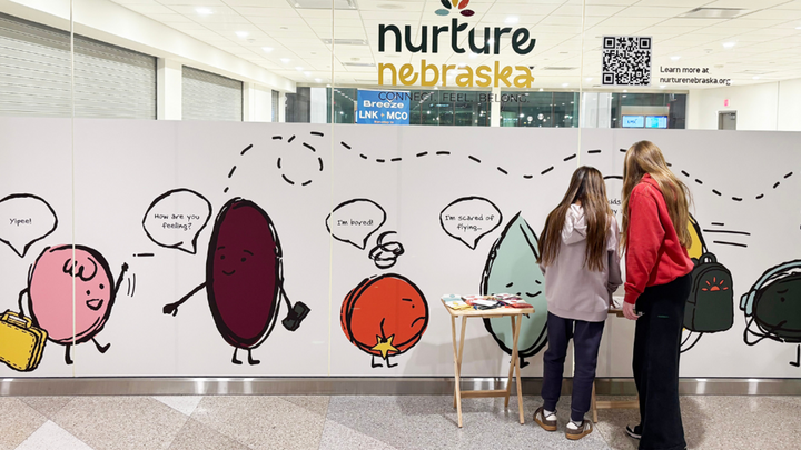 two travelers look at a large display about Nurture Nebraska at the Lincoln Airport