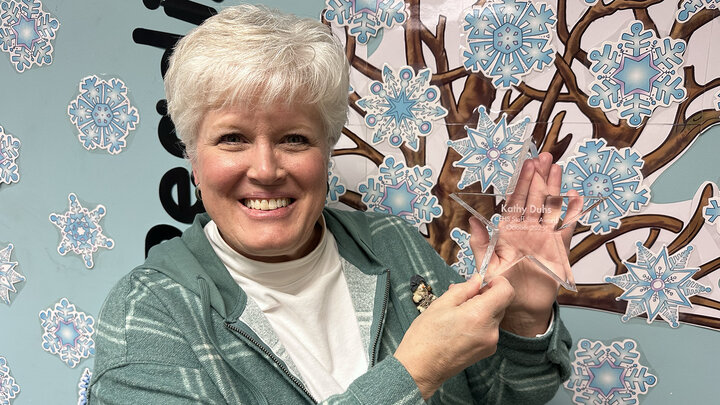 Kathy Duhs holds her Staff Star award with a blue and snowflake wall behind her