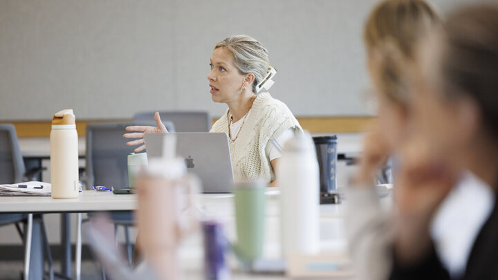 Jillian Harpster sits a table with her laptop open while speaking during one of her classess