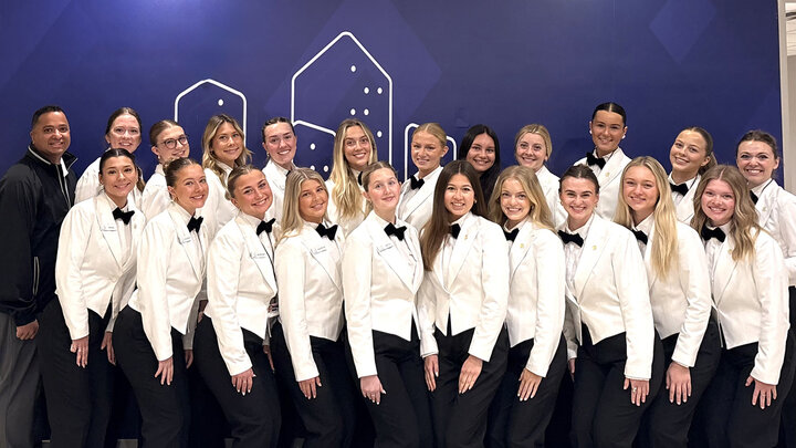 group photo with two rows of 21 students wearing white jackets and black pants with black bow ties, faculty leader Ajai Ammachathram in black shirt and gray pants on left back row