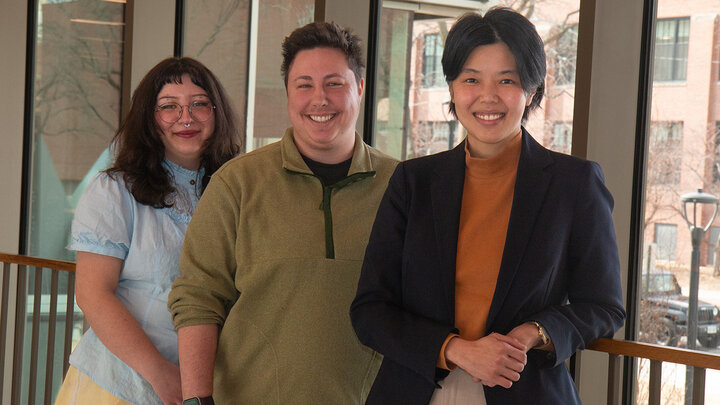 Davianna Daydreamer and Jace Meunier, graduate research assistants, and Mun Yuk Chin, assistant professor of counseling psychology, stand in a row and smiling with a window looking out onto 14th Street in the background