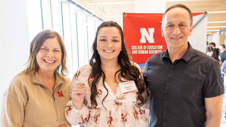 Bryanne Mieth poses for a photo with her parents, Carla Mieth and Bruce Mieth, near a banner for the College of Education and Human Sciences after the Teacher Education Convocation ceremony.