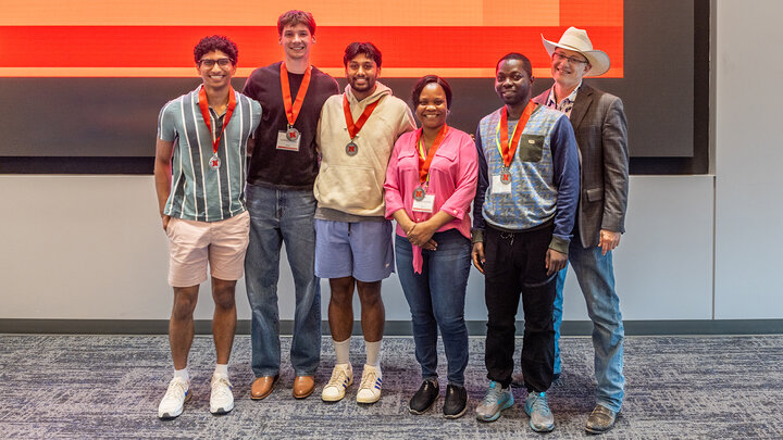 five students stand together wearing medals for winning The Great Prairie AI Show; Guy Trainin, professor of teaching, learning and teacher education stands on the right side of the students wearing a cowboy hat, suit jacket and boots