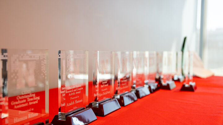 Glass awards arranged in a row on a red tablecloth near a bright window in Carolyn Pope Edwards Hall.
