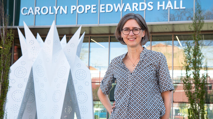 Caroline Villiger poses outside Carolyn Pope Edwards Hall with a large lotus sculpture in the background in front of the building. (Kyleigh Skaggs, Kindred Media)