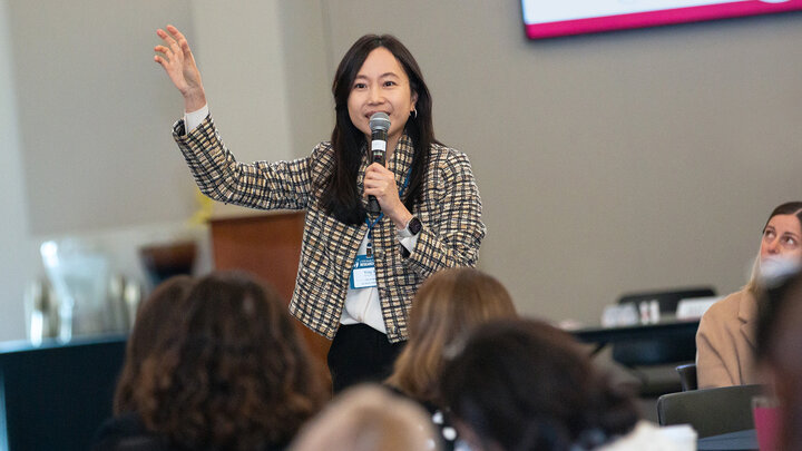 Ying Xu, assistant professor of education in the Harvard University Graduate School of Education, holds a microphone in her left hand and gestures in the air with her right hand while presenting the keynote speech at the 2026 CYFS Early Childhood Research Summit.