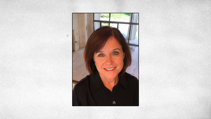 gray textured background with centered headshot of Cathy Gabell wearing black shirt and standing on second floor of large room with white marble and glass doors in background
