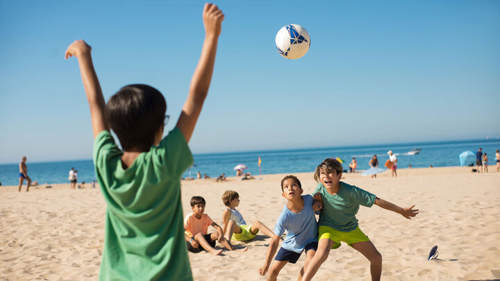 Children playing beach volleyball under a sunny blue sky.