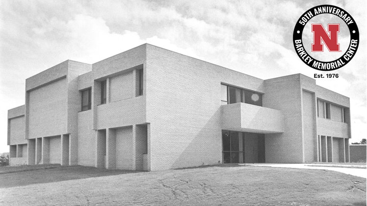 Brick building with angular design on a grassy lawn in black and white; red, black and white circular logo celebrating 50th anniversary in upper right.