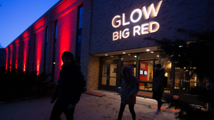 Photo at nighttime of a brick building lit up red. A light projects 