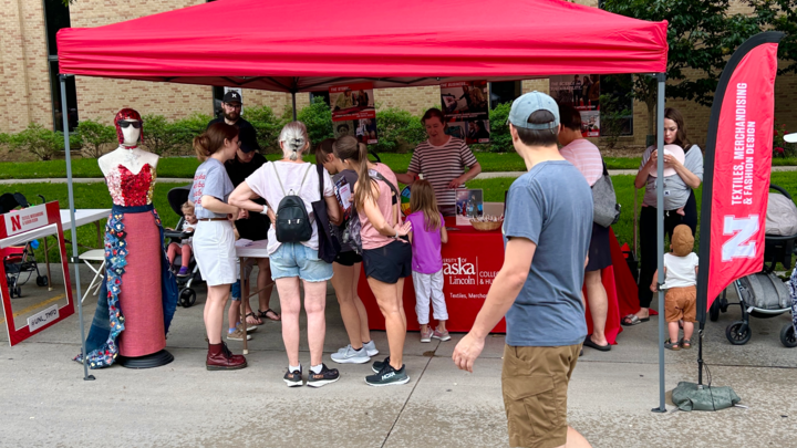 A large group gathers at the Textiles, Merchandising and Fashion Design red tent at East Campus Discovery Days. The display features the button dress community project.