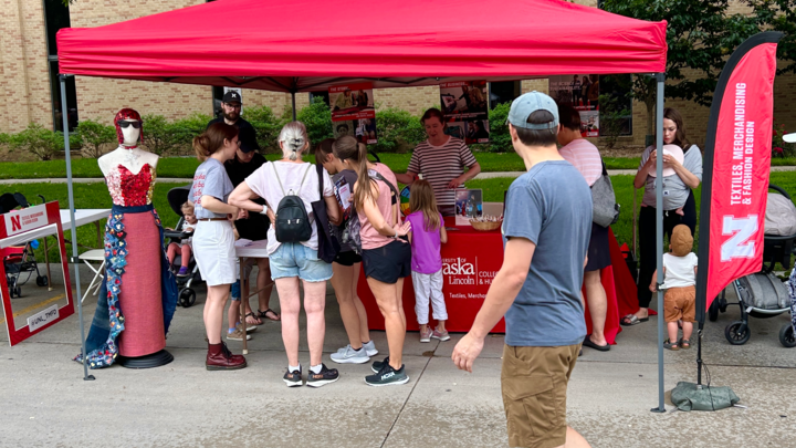 A large group gathers at the Textiles, Merchandising and Fashion Design red tent at East Campus Discovery Days. The display features the button dress community project. 