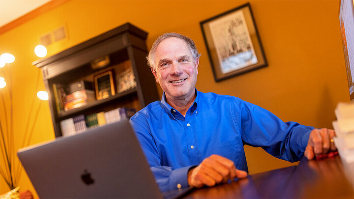 Ken Kiewra sits at a desk in front of a laptop computer. 