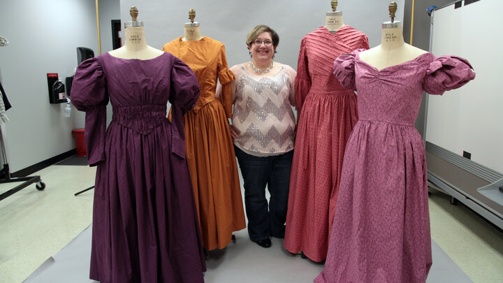 Heather Striebel stands in the middle of four dresses hanging on mannequins. 