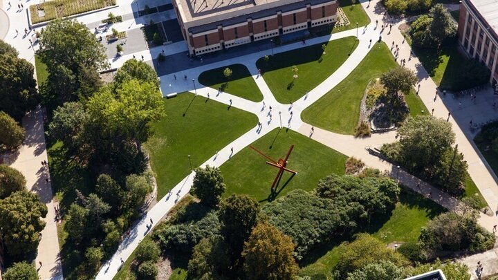 Overhead view of campus landscape. People walking on sidewalks that come together near the center of the photo. 