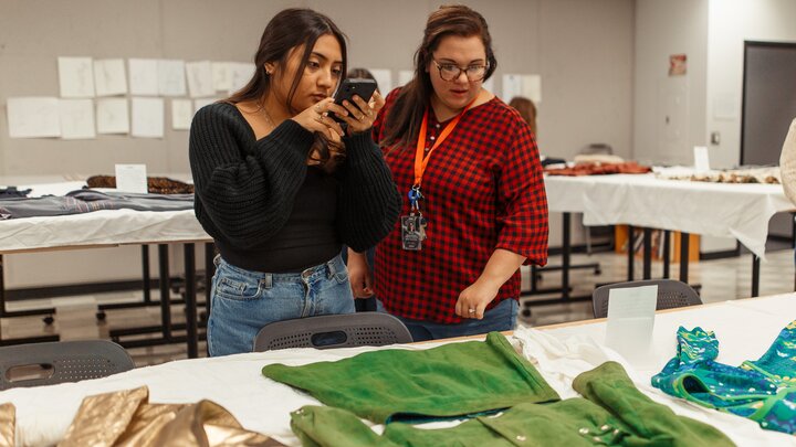 South High student takes a photo using her smartphone of a green garment from the Historical Textiles Collection housed in the department of Textiles, Merchandising & Fashion Design. 