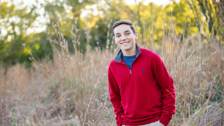 Grant Cline, wearing a red and blue sweatshirt, stands in a field of tall grass.