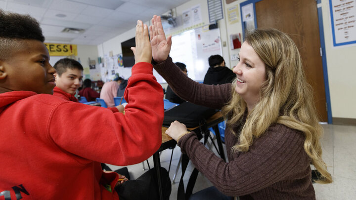 An adult and child smiling and high-fiving in a classroom setting. 