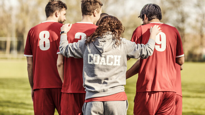 Three athletes wearing red jersey's walk with their coach, wearing a gray hooded sweatshirt.