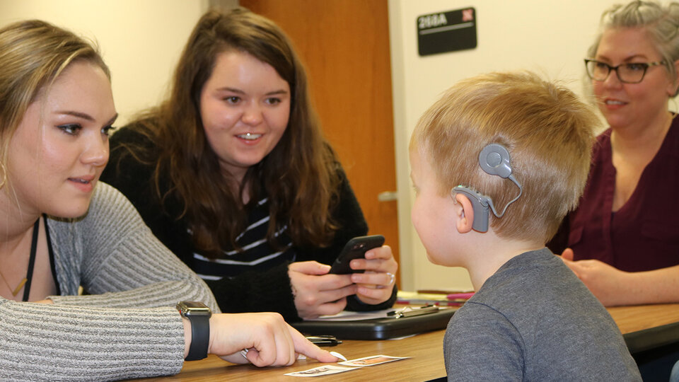 Child with hearing aid conversing with women.