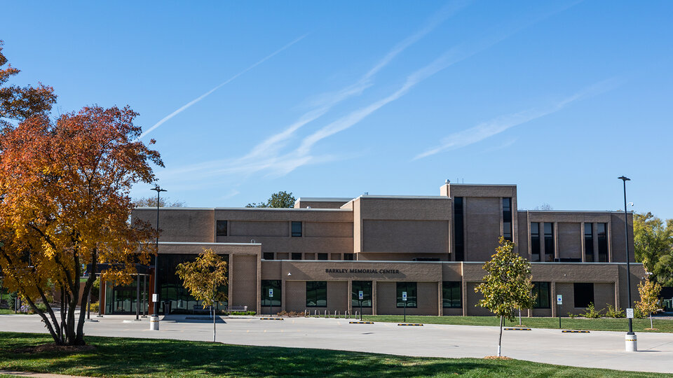 Brick building with large windows, trees with autumn leaves, and a clear blue sky.