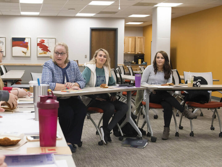 Instructor sitting discussing topics with college age students.