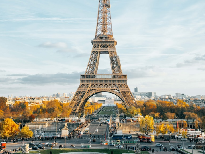 Eiffel Tower framed by autumn trees under a partly cloudy sky in Paris.