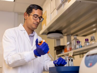 Scientist wearing gloves and lab coat uses pipette in a laboratory setting.