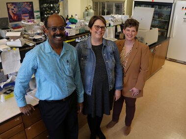Three people in a lab, surrounded by scientific equipment and supplies