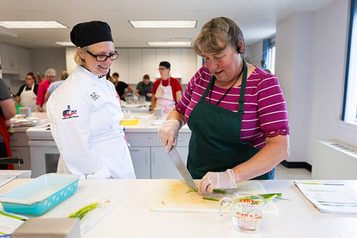 Brenda Windmuller stops to chat with Renee Cornett, food and nutrition services operations manager for Gretna Public Schools, as she cuts thin strips into green onions. Windmuller worked with school nutrition professionals from across the state during the 2025 Child Nutrition Training Academy. She said many participants were repeat attendees, returning to build on the skills learned in previous years – ranging from knife skills to financial planning to recipe development and more – and to connect with peers
