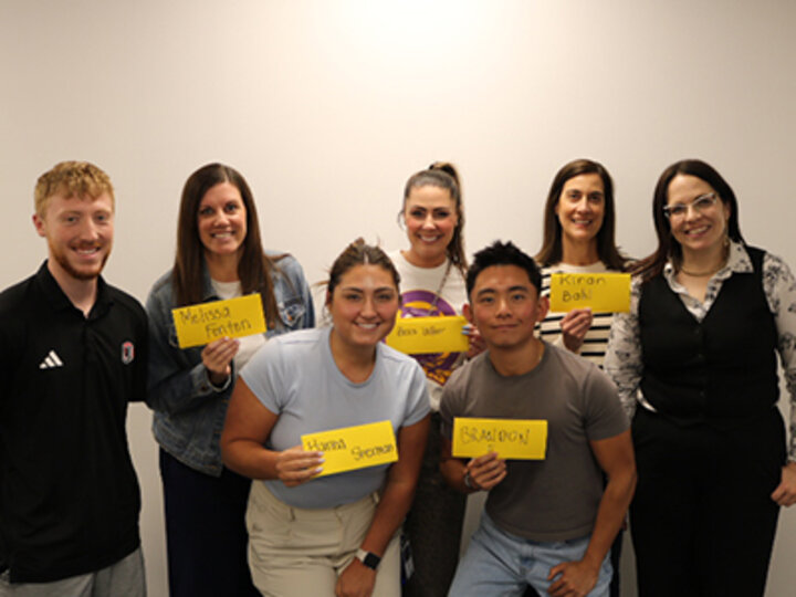 six panelists and Erin Pfister stand with five people in the back row and two in the front for a group photo against a light-colored wall
